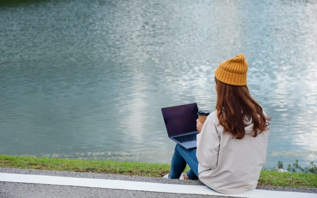 A young woman using and working on laptop computer while traveling mountains and lake
