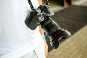 Câmera fotográfica no pescoço de um homem com roupa branca.