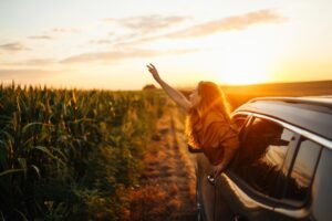 Happy woman outstretches her arms while sticking out car window. Lifestyle, travel, tourism, nature.