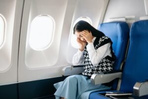 Photo of a frustrated woman sitting on an airplane with her head in her hands.