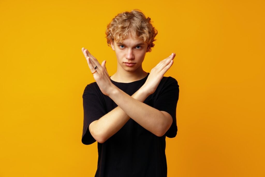 Photo of young strict man showing arms denial symbol against yellow background