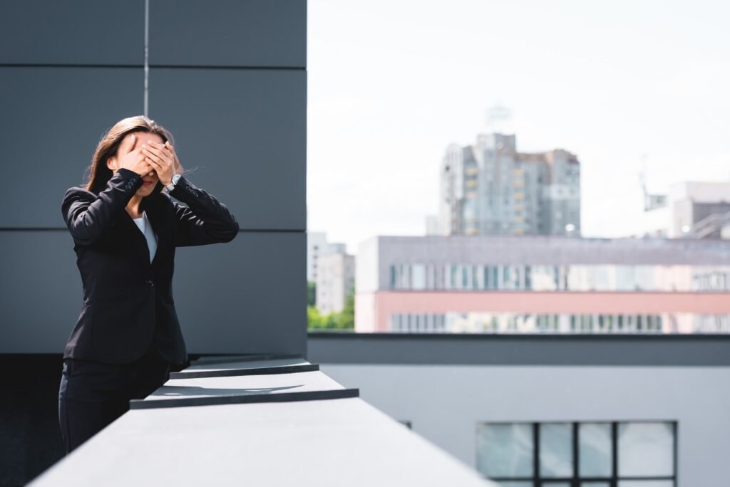 young businesswoman, suffering from fear of heights, standing on rooftop and covering face with