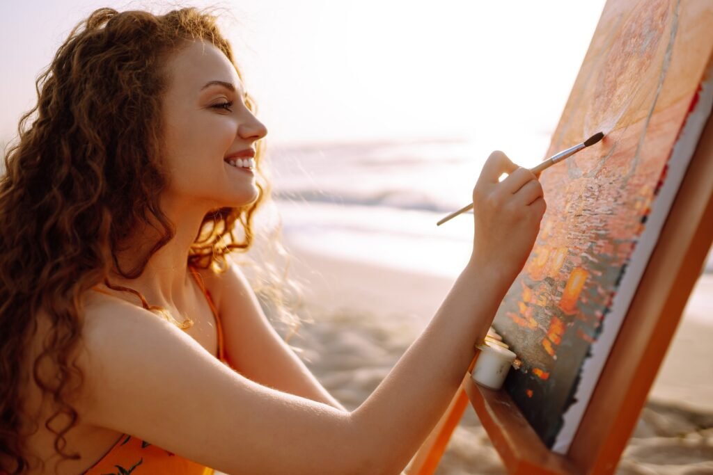 Young female artist drawing the picture at the beach. Hobby and leisure concept