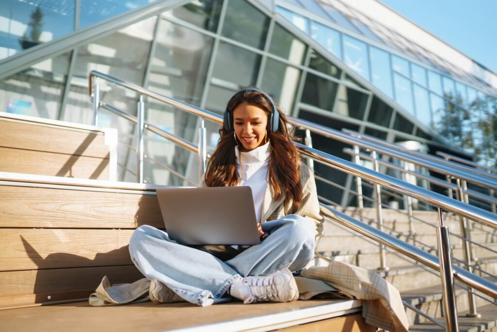 Young woman in headphones with laptop on city street. Video conference. ?nline training. Freelancer