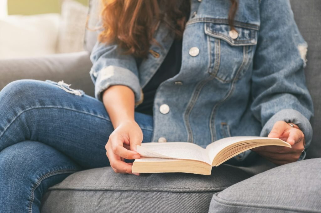 Closeup image of a woman sitting and reading a vintage novel book on sofa