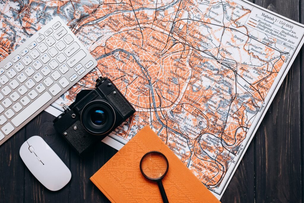 Keyboard, computer mouse, maps, notebook and camera, holiday travel plans.