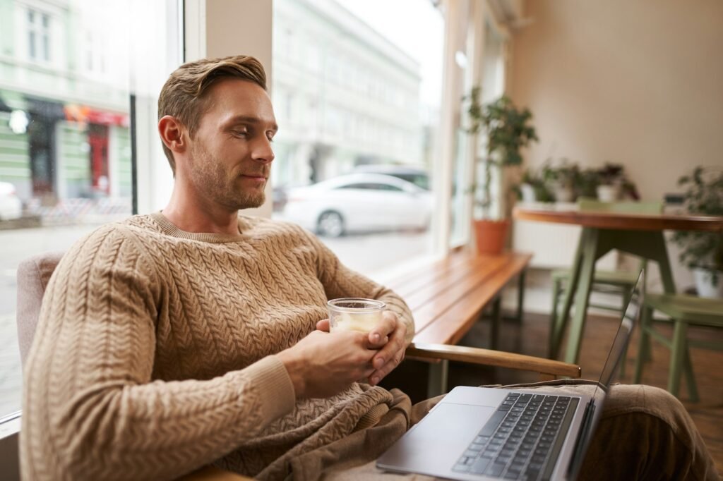 Portrait of male entrepreneur, digital nomad sitting in cafe with glass of cappuccino, looking at