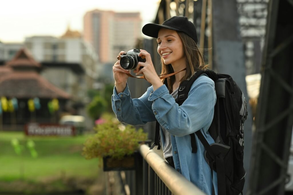 Cheerful female travel blogger recording video vlog with camera while standing on bridge