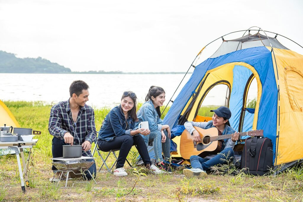 group of traveling friends relax, pitch tent play guitar and cook dinner by lake